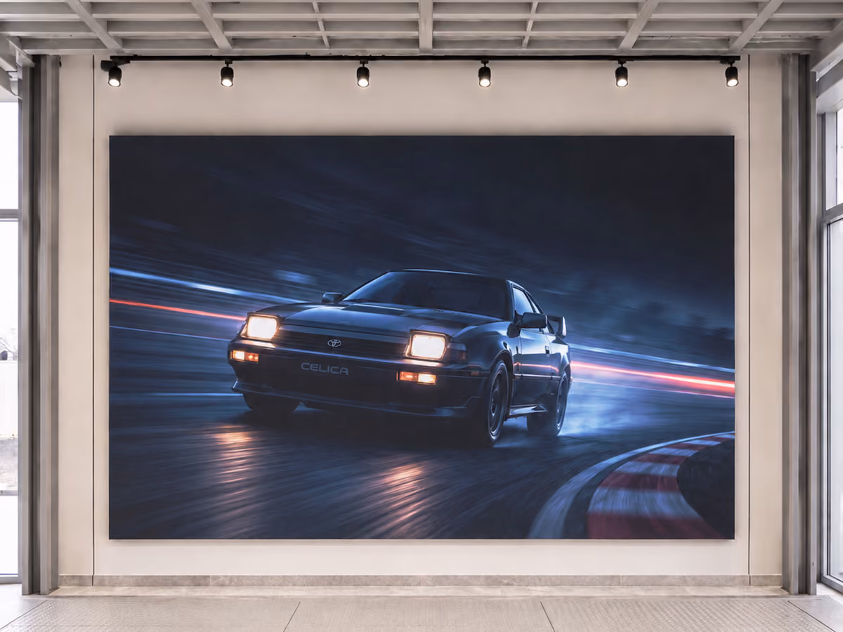 Large Video Wall with an image of a black Toyota Celica with pop-up headlights turning on a race track at night, with motion blur and light trails, displayed in a modern gallery room with white walls and overhead track lighting.