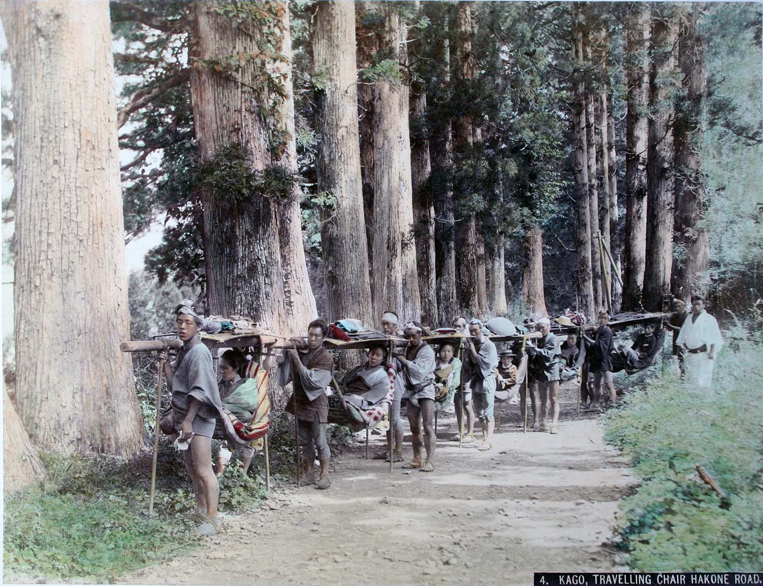 A hand-coloured historic photograph of travelers carried in kago palanquins along the cedar-lined Hakone road