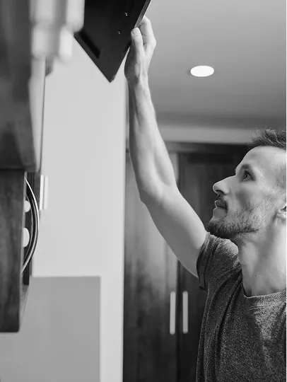 Man in a t-shirt reaching up to open an overhead cabinet in a kitchen.