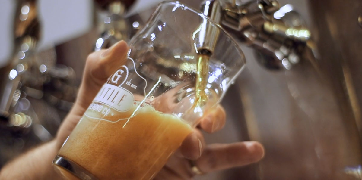 Close-up of a hand holding a tilted glass as dark beer pours from a tap.