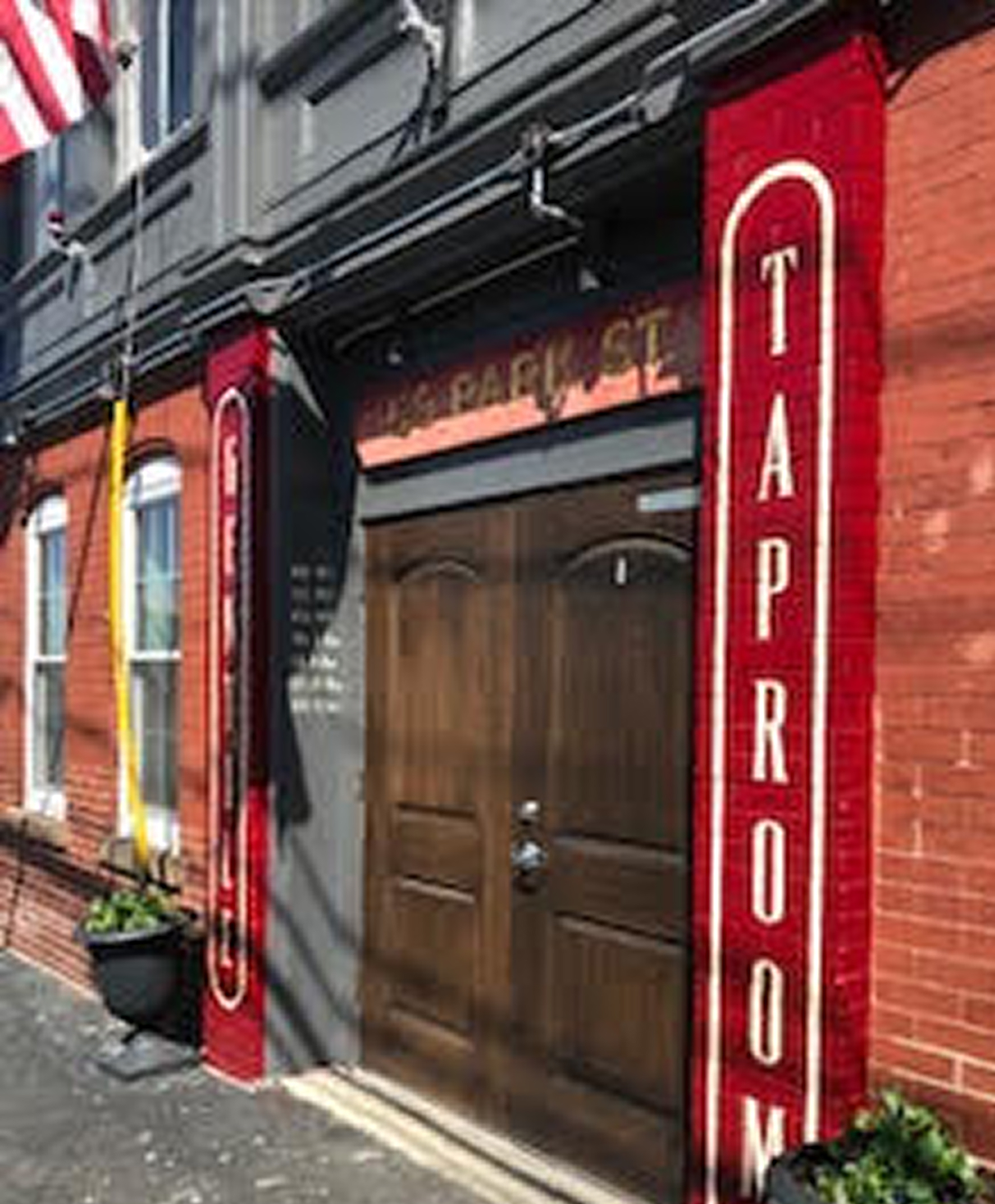Entrance to Taproom with wooden double doors and red vertical signs on brick building.