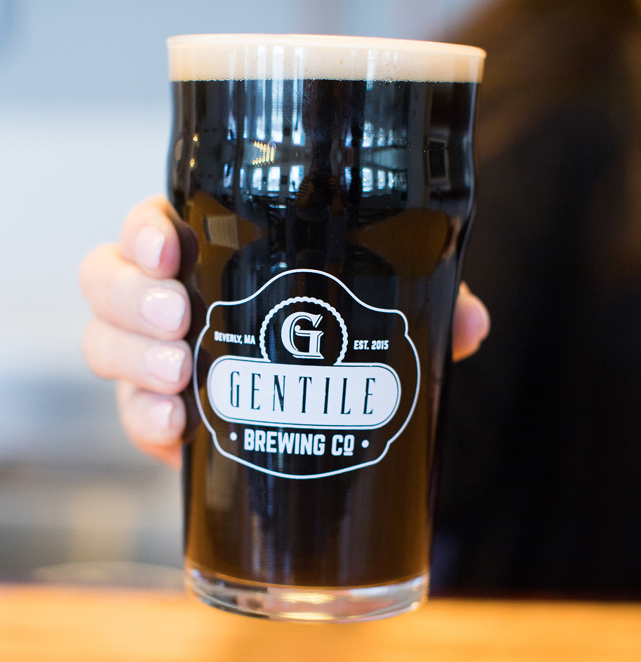 Hand holding a pint glass of dark beer with Gentile Brewing Co logo on it.
