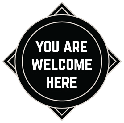Black badge with white text saying 'YOU ARE WELCOME HERE' inside a circle with decorative diamond shape.