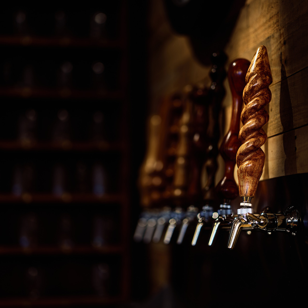 Close-up of wooden beer tap handles on a bar with dimly lit shelves in the background.