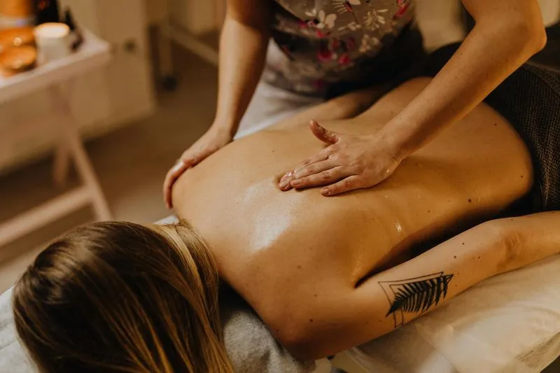 Massage therapist massaging a woman's oiled back in a spa setting