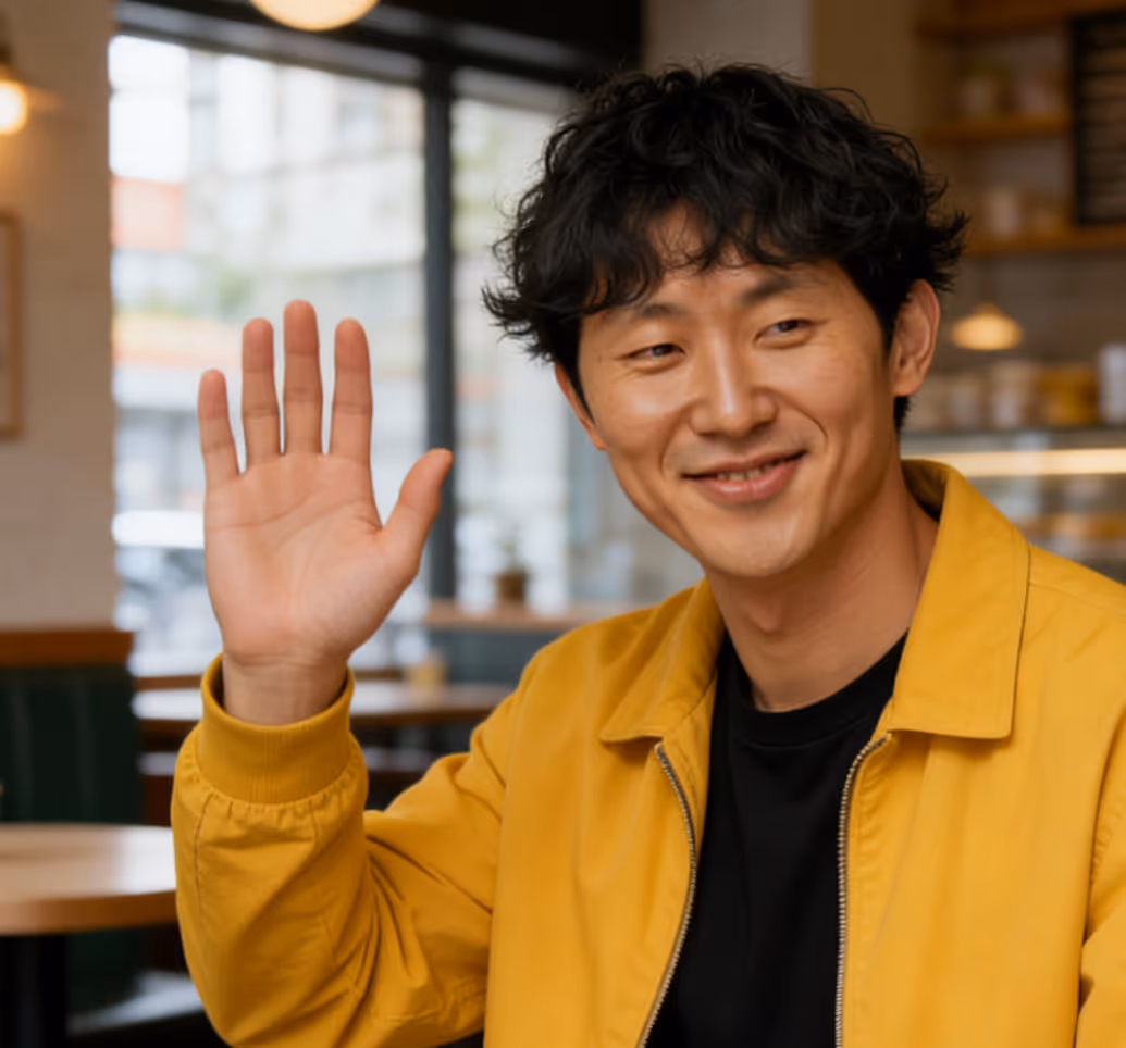 A headshot of a smiling Asian man with curly hair wearing a gray tweed jacket over a black shirt
