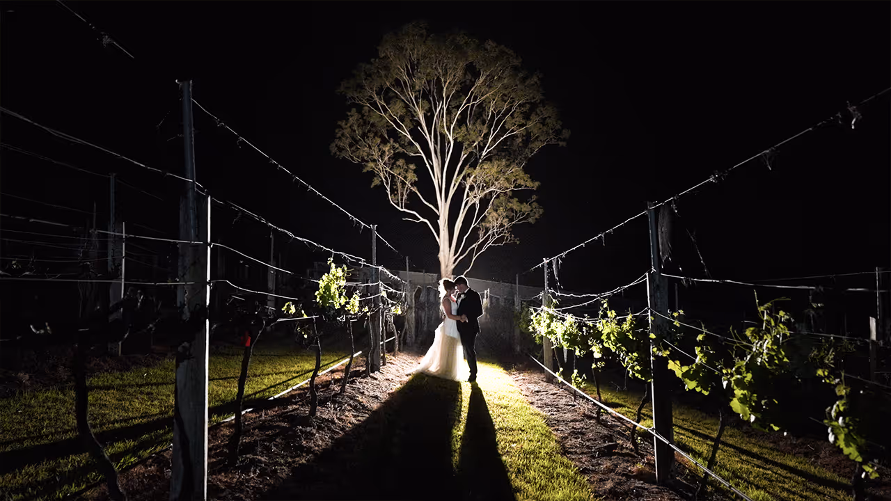 Bride and groom share a romantic moment under a spotlight in a vineyard at night, captured in cinematic style by Creo Bella.