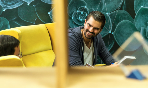 Two individuals converse in a modern workspace with vibrant seating and abstract wall art.