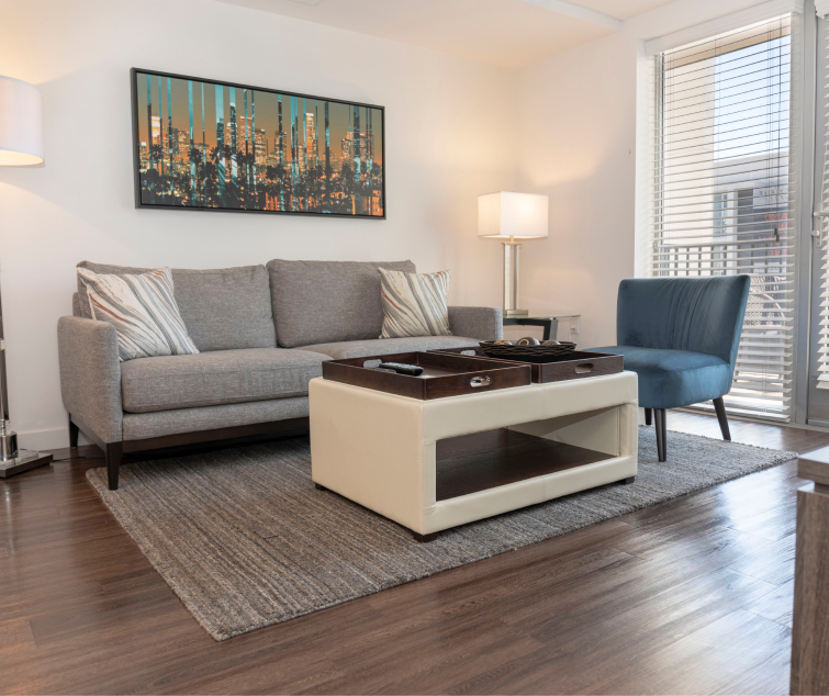 A modern living room with a gray sofa, blue chair, and a beige coffee table on a textured rug.