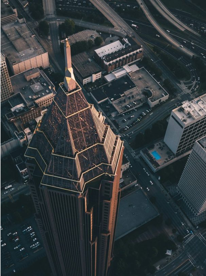 Aerial view of a tall, gold-tipped skyscraper surrounded by urban streets and buildings at dusk.