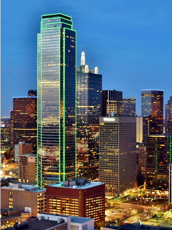 A vibrant cityscape featuring a tall, green-lit skyscraper at dusk in downtown Dallas, Texas.
