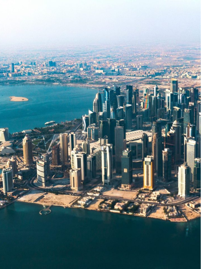 Aerial view of a modern city skyline with skyscrapers by the waterfront and expansive urban sprawl.