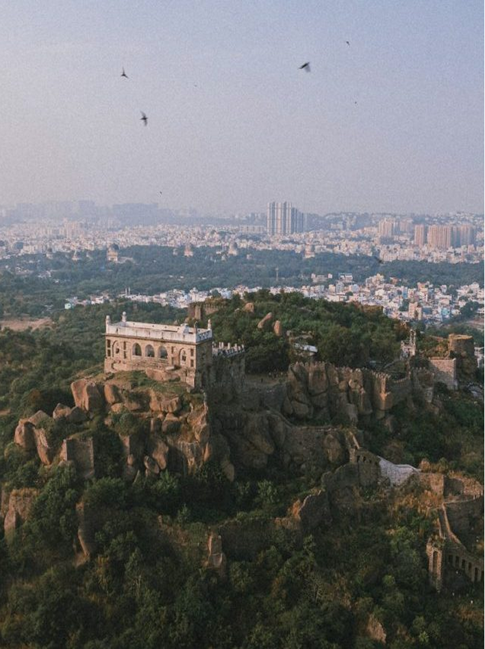 A historic fort atop rocky terrain overlooks a sprawling urban cityscape under a clear sky.