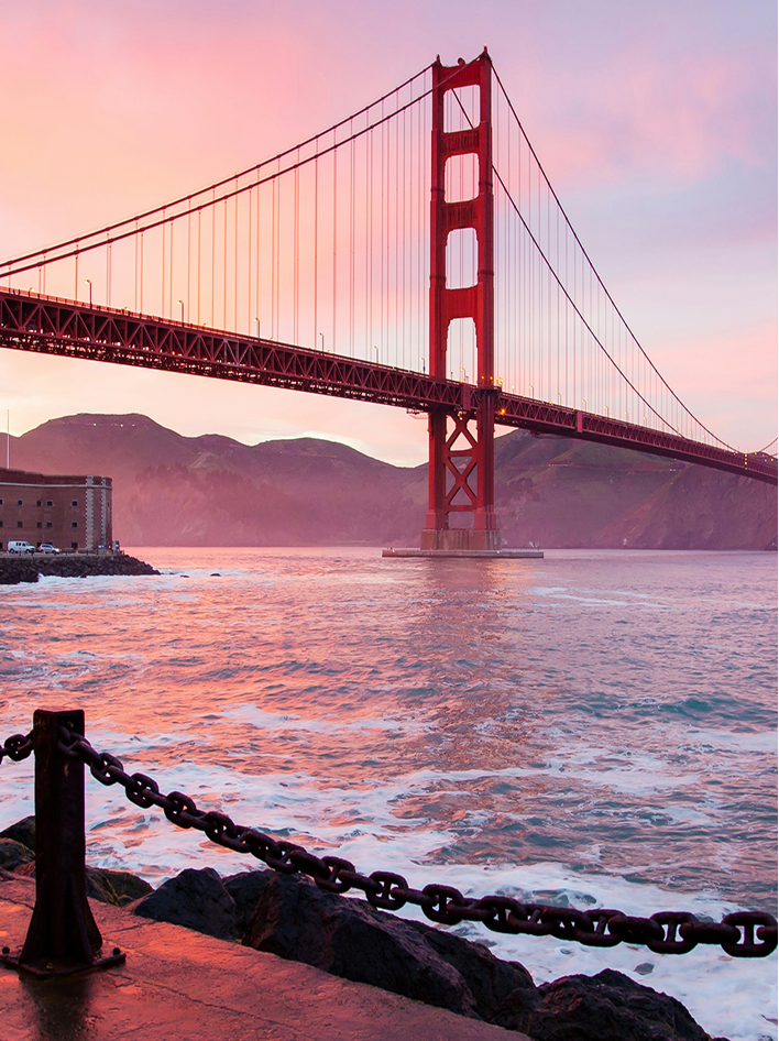 Golden Gate Bridge at sunset, with vibrant skies and waves crashing against the rocky shoreline.