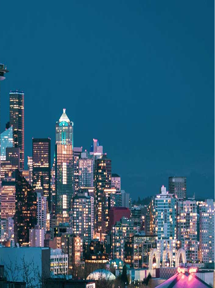 A vibrant city skyline at night, illuminated by glowing lights against a deep blue sky.