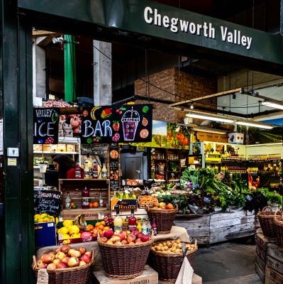 Chegworth Valley market stall displays fresh produce, juices, and vibrant fruits in a rustic setting.