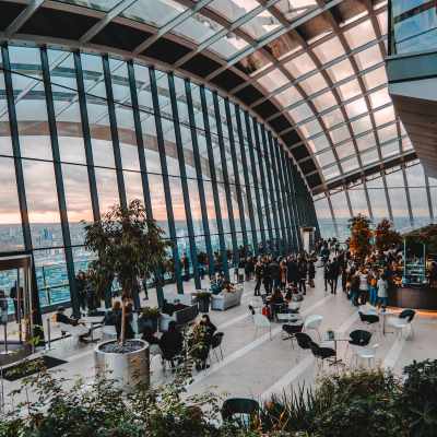 A modern glass atrium with lush greenery, seating areas, and people enjoying the space.