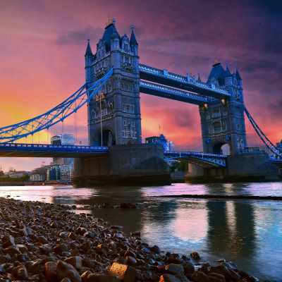 Tower Bridge at sunset, reflecting in the Thames with a rocky foreground.