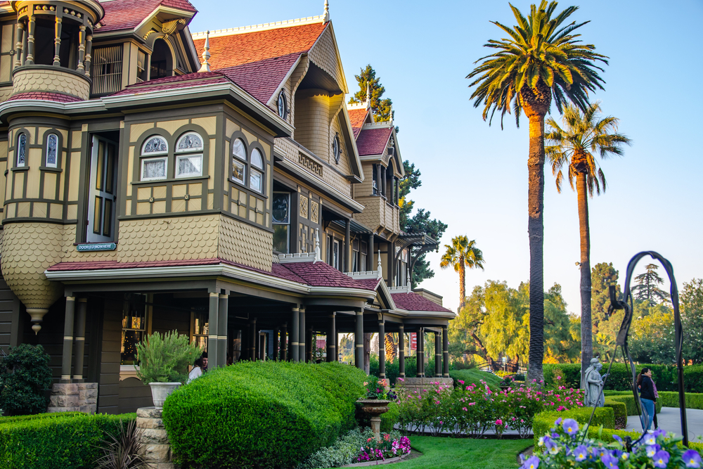 The Winchester Mystery House features ornate architecture, lush gardens, and palm trees.