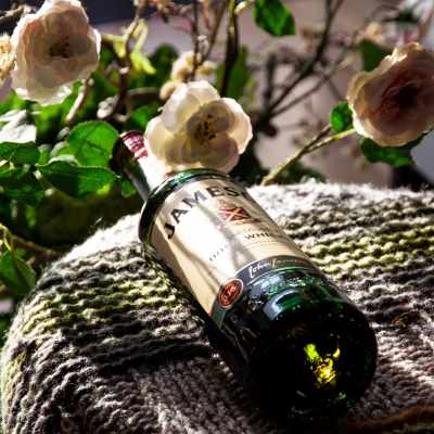Jameson Irish Whiskey bottle resting on textured fabric, surrounded by blooming white roses.