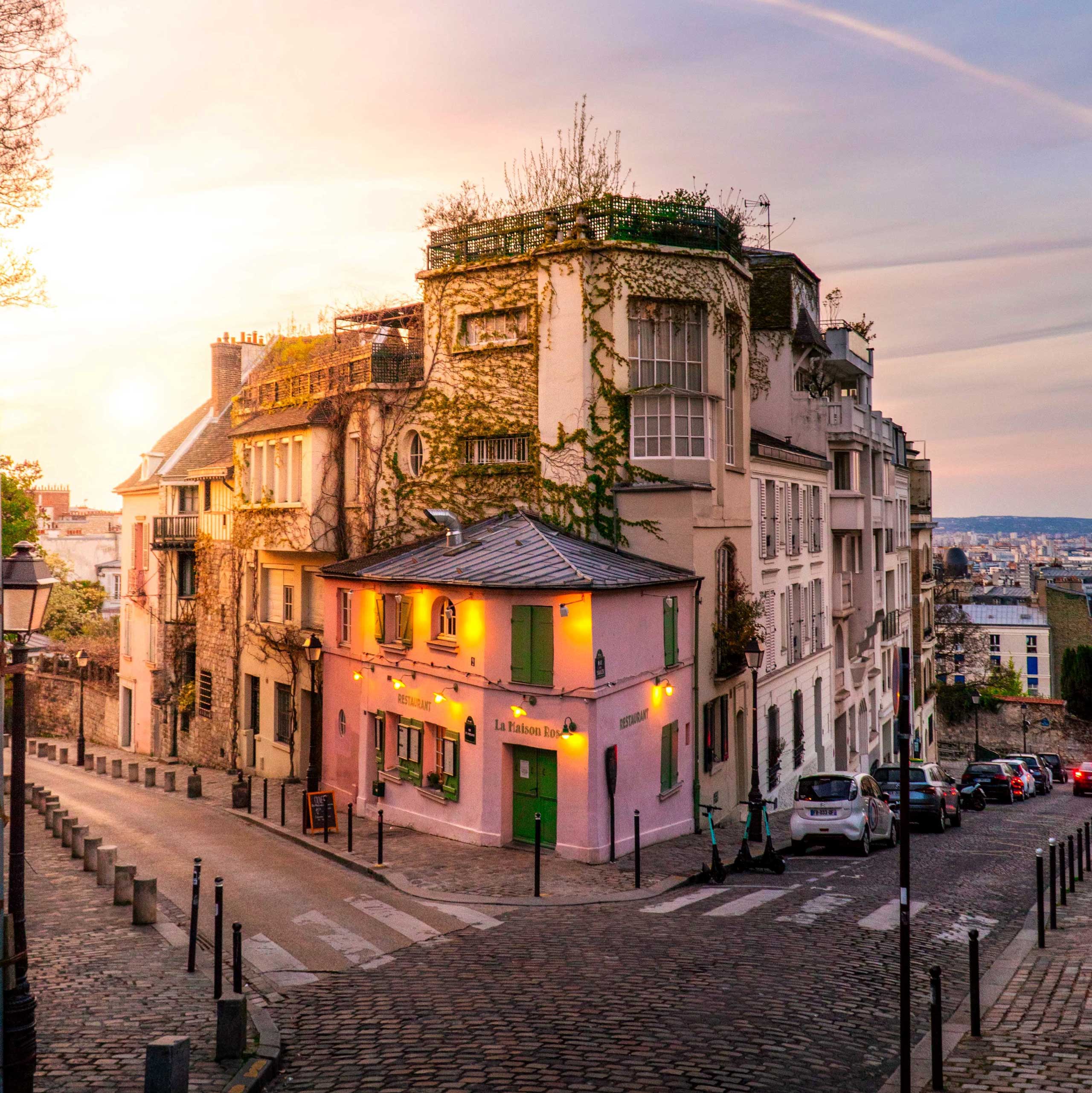 A charming pink café, "La Maison Rose," sits on a cobblestone street in Montmartre at sunset.
