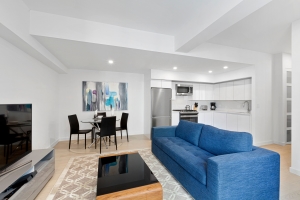 Modern open-concept living space with a blue sofa, dining area, and sleek white kitchen.