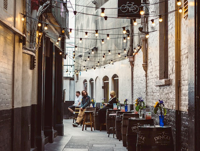 A narrow alleyway with string lights, outdoor seating, and people enjoying a casual atmosphere.
