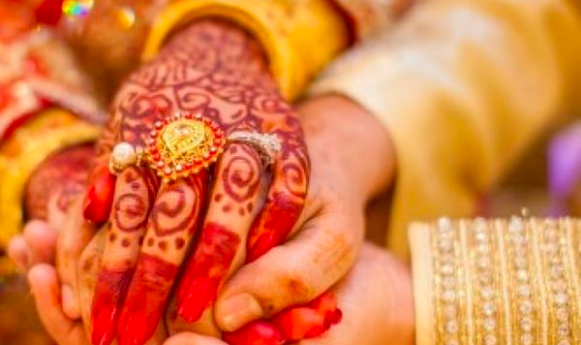 Henna-adorned hands of a bride, clasped by the groom, symbolizing a traditional wedding ritual.