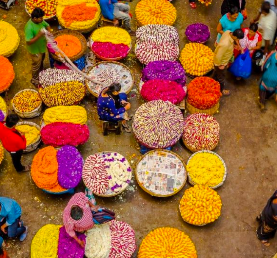 A vibrant flower market with colorful blooms arranged in baskets, surrounded by vendors and buyers.