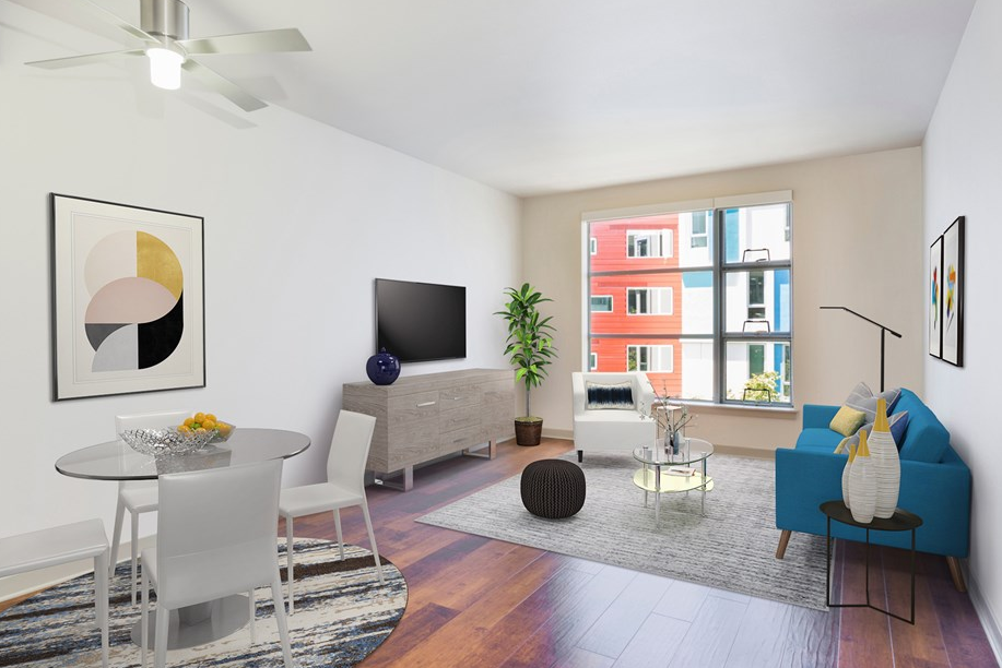 Modern living room with bright decor, wood flooring, and large window overlooking colorful buildings.