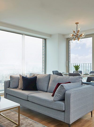 Modern living room with a gray sofa, large windows, and a stylish chandelier.