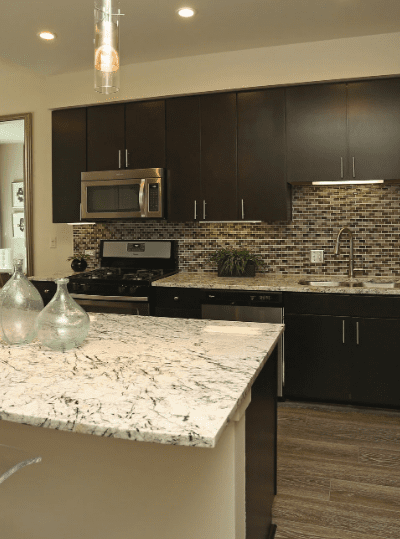 Modern kitchen with dark cabinets, mosaic backsplash, and marble-patterned countertops.