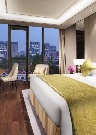 Elegant hotel room with city view, featuring modern decor, large windows, and warm lighting.