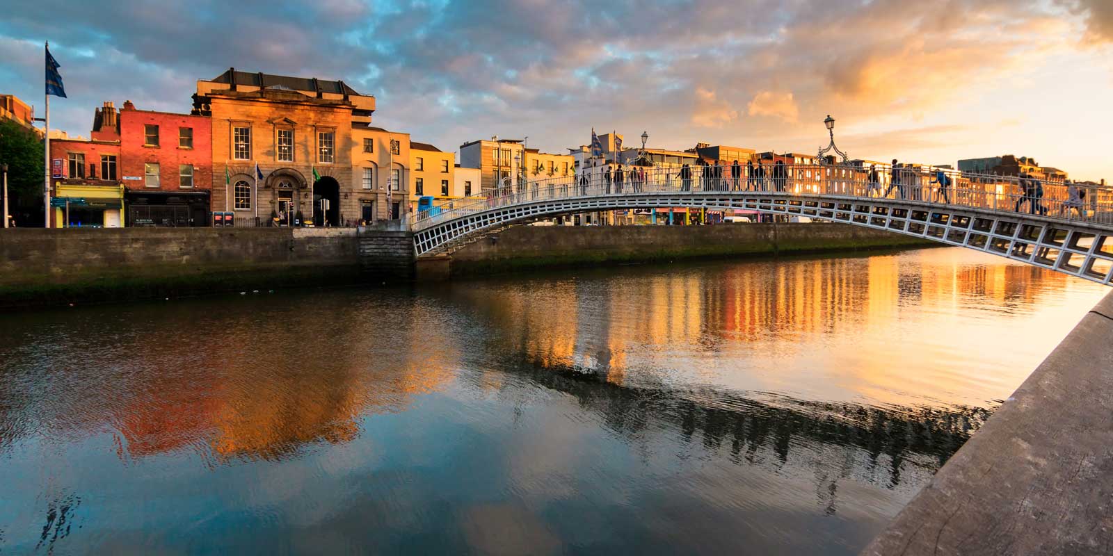 Ha'penny Bridge spans the River Liffey in Dublin, reflecting warm sunset hues on the water.