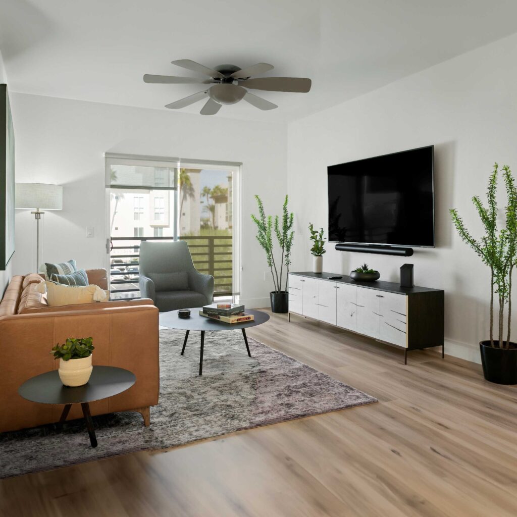 Modern living room with neutral tones, sleek furniture, large TV, and natural light.