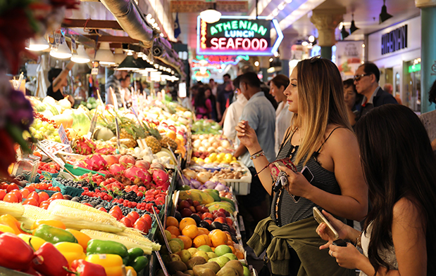 A vibrant market scene with fresh produce and seafood, bustling with shoppers under neon signage.