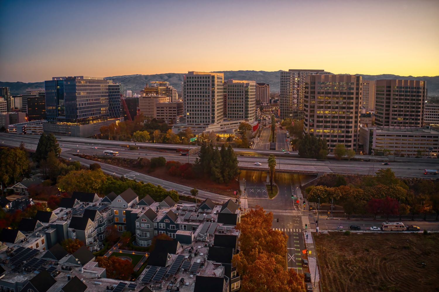A cityscape at sunset featuring modern buildings, highways, and residential areas.