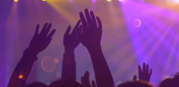 Silhouetted hands raised in a vibrant, colorful concert or event lighting atmosphere.
