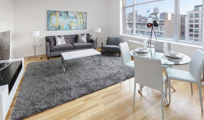 Modern living room with gray sofa, glass dining table, large window, and cityscape view.