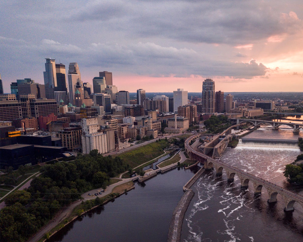 Minneapolis skyline at sunset with the Stone Arch Bridge and Mississippi River in the foreground.