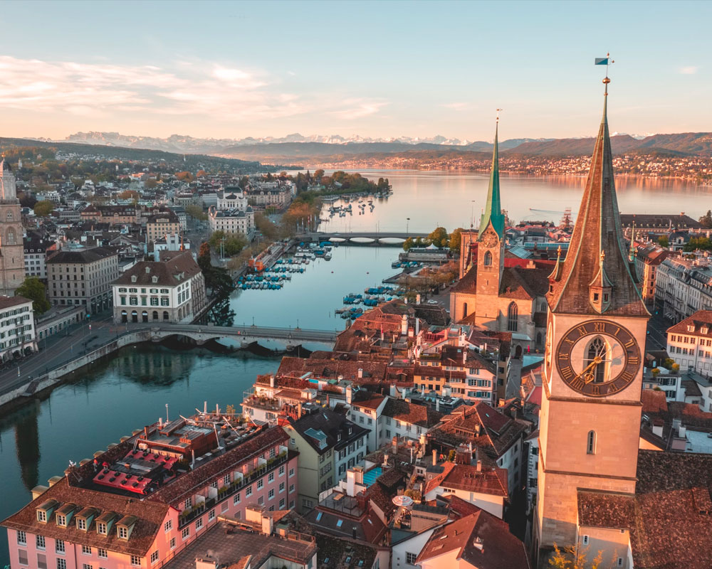 Aerial view of Zurich's historic center, Lake Zurich, and the Alps in the background at sunset.