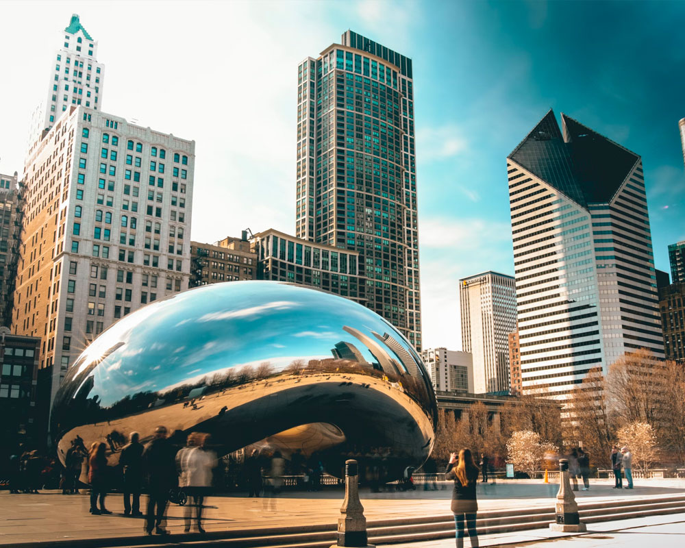 Cloud Gate sculpture in Chicago's Millennium Park, surrounded by skyscrapers and visitors.
