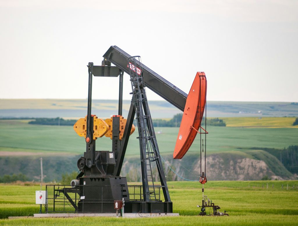 Oil pumpjack operating in a green field with rolling hills in the background.