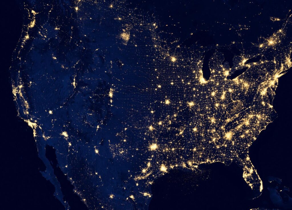 Satellite view of the U.S. at night, showing illuminated cities and infrastructure networks.