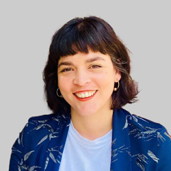 A person with short, dark hair wearing a patterned blazer and white shirt against a gray background.