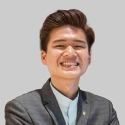 A person in formal attire with neatly styled hair, wearing a gray suit and light shirt.