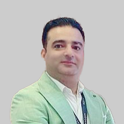 A person wearing a light green blazer and white shirt, accessorized with a lanyard.