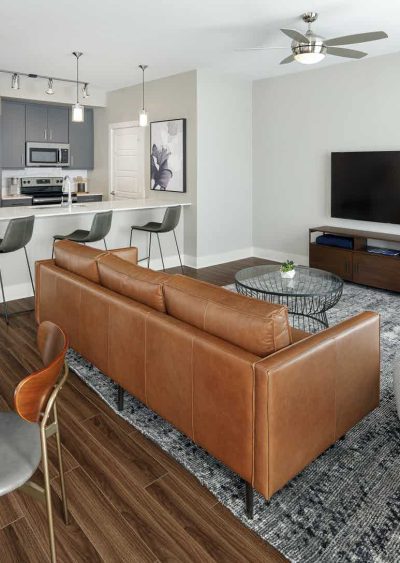 Modern living room with leather sofa, open kitchen, and sleek decor in neutral tones.