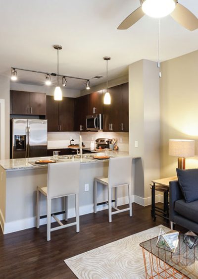 Modern kitchen with dark cabinets, pendant lighting, and a small dining area with bar stools.