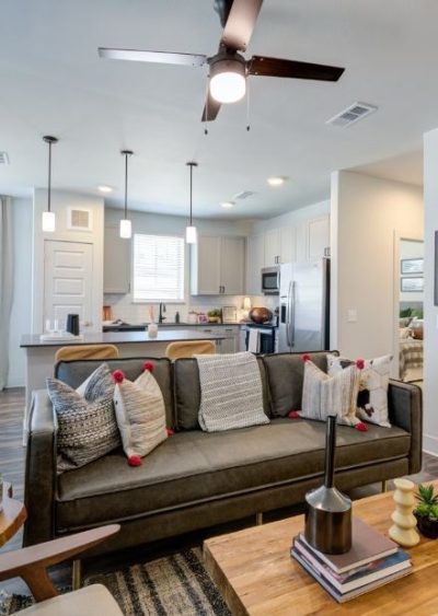 Modern open-concept living space with neutral tones, cozy decor, and a kitchen in the background.